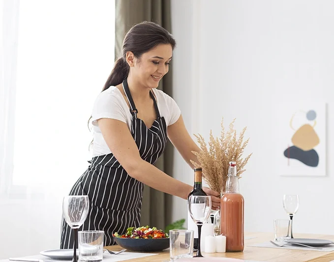 [:en]Haushälterin stellt Trockenblumen auf einen Esstisch[:]